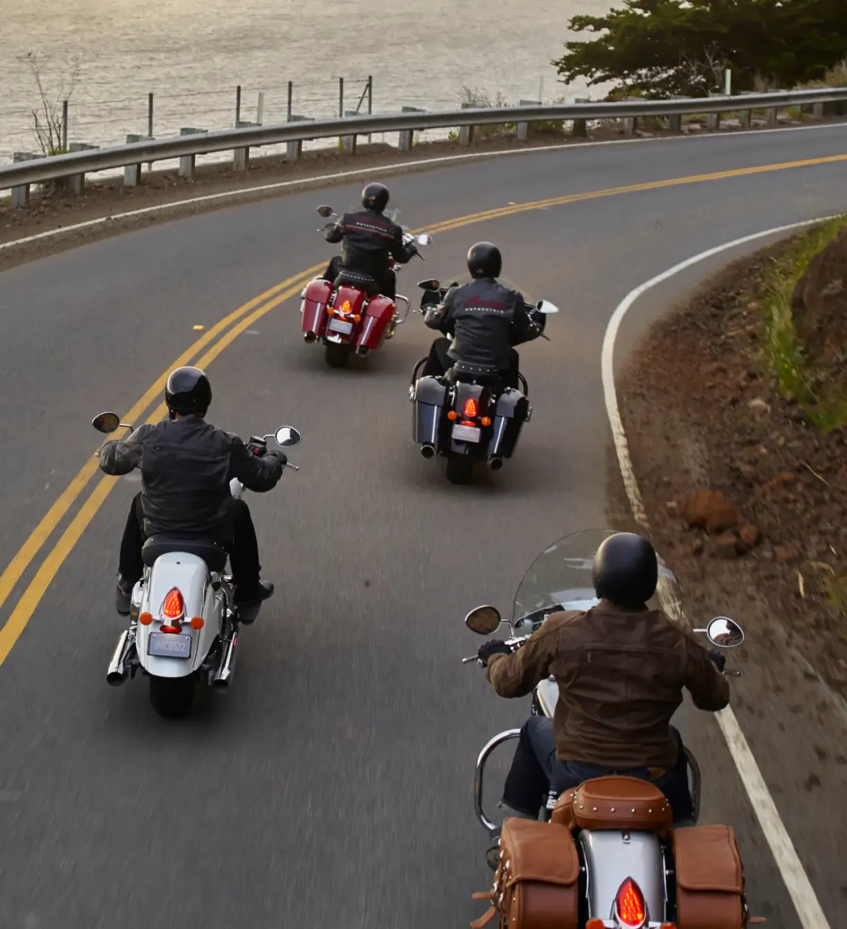 Group of people riding Indian motorcycles up a coastal road.